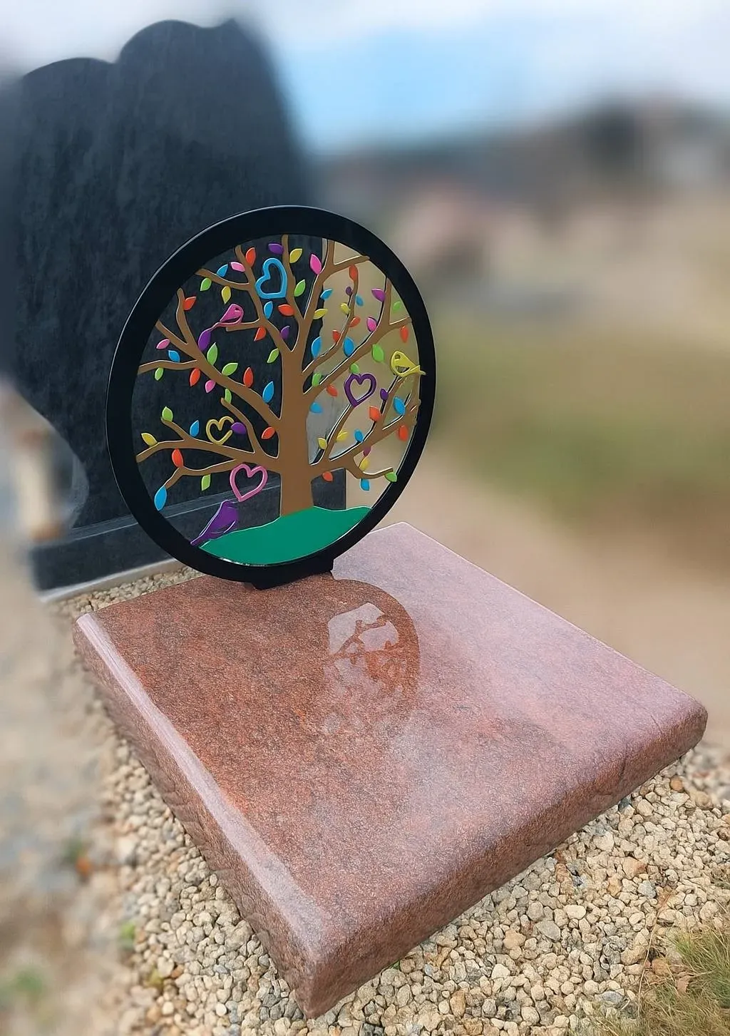 Plaque funéraire moderne en granit rose avec motif d'arbre de vie coloré.